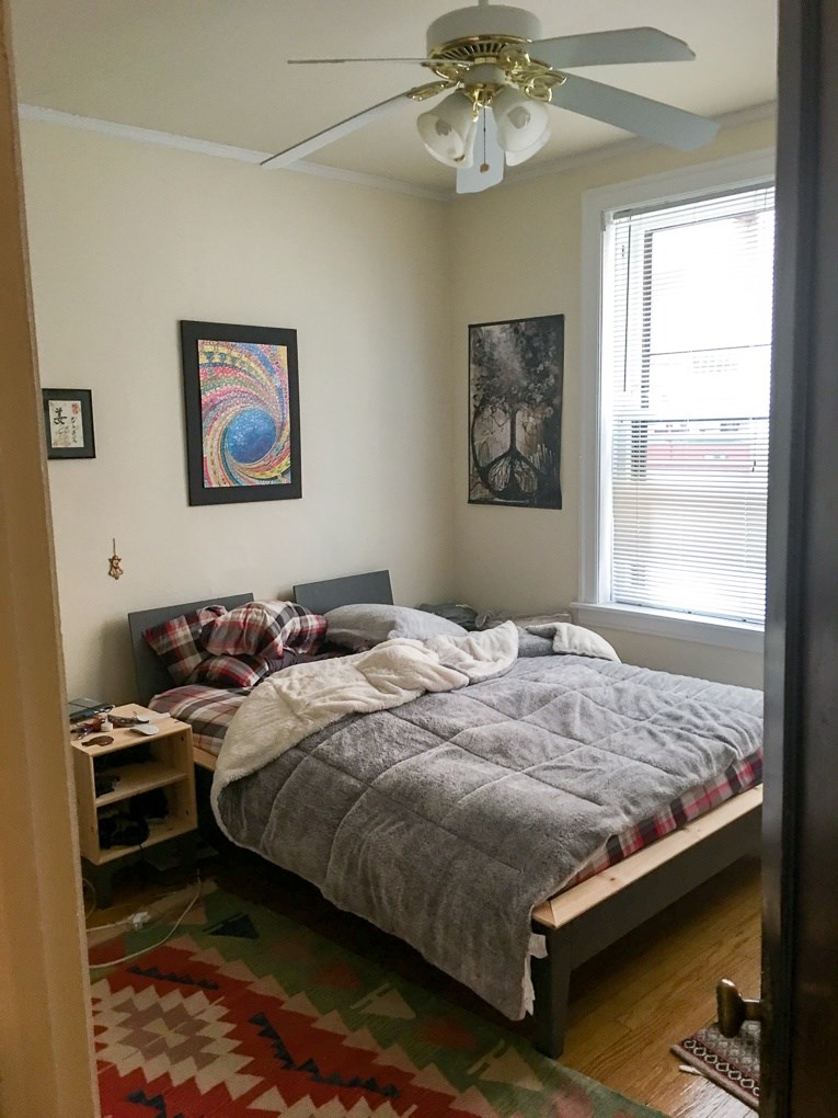 A bedroom with a bed, a ceiling fan, and two pictures on the wall.