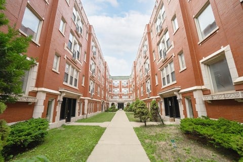 a walkway between red brick apartment buildings with grass and bushes