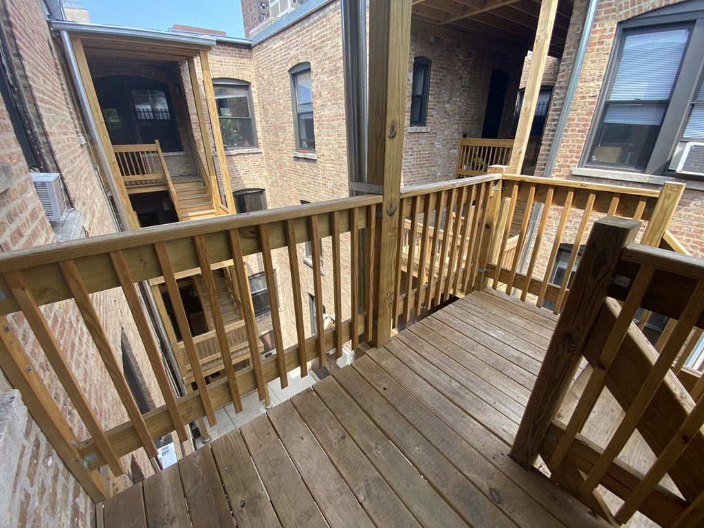 the back deck of a brick apartment building with a wooden railing