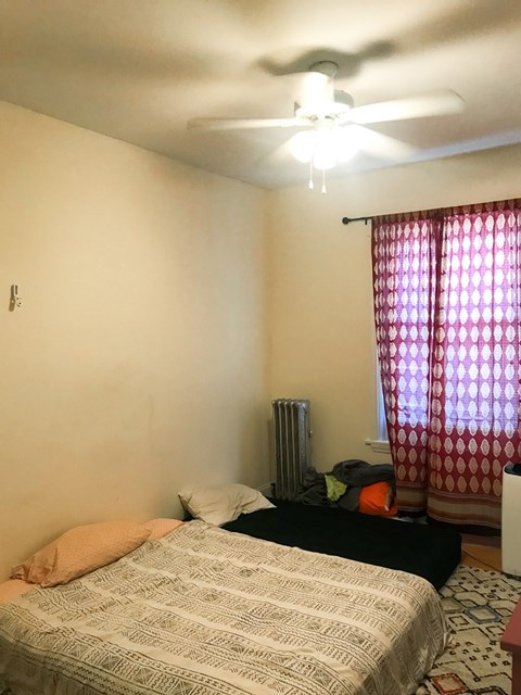 A bedroom with a bed, a ceiling fan, and a window with curtains.