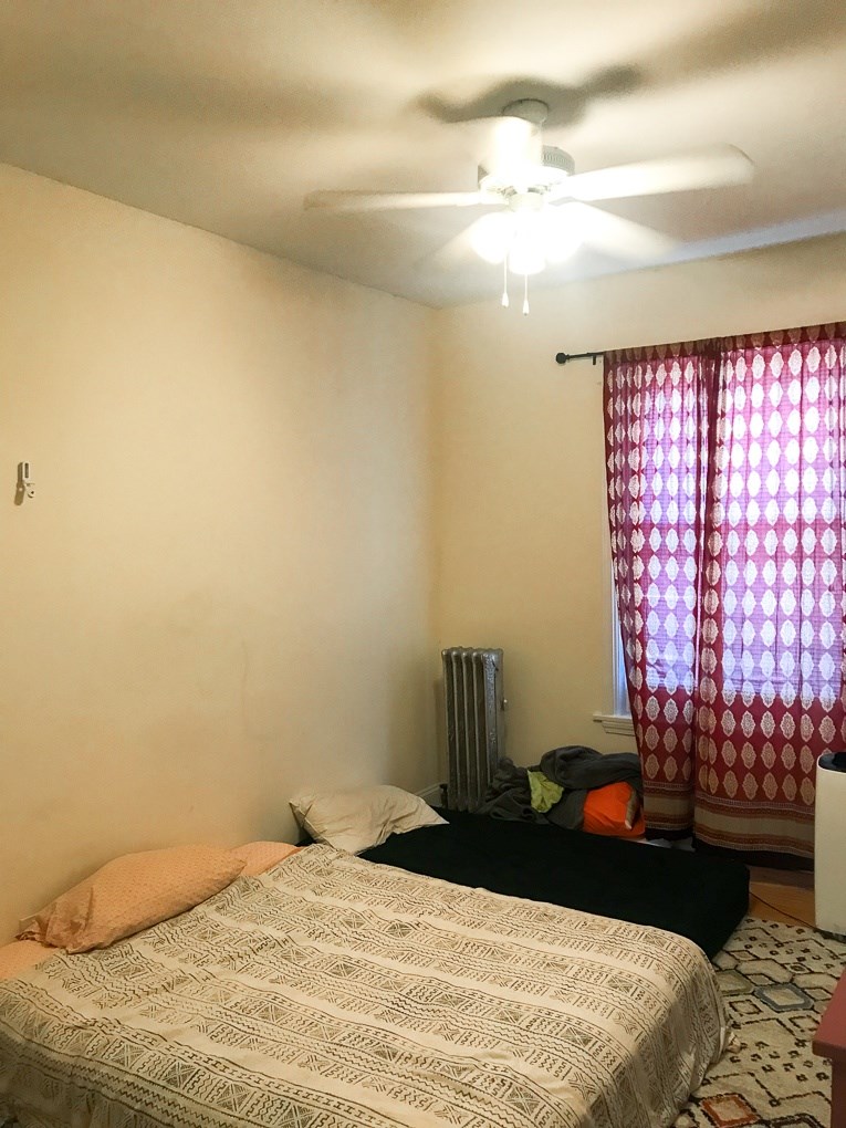 A bedroom with a bed, a ceiling fan, and a window with curtains.