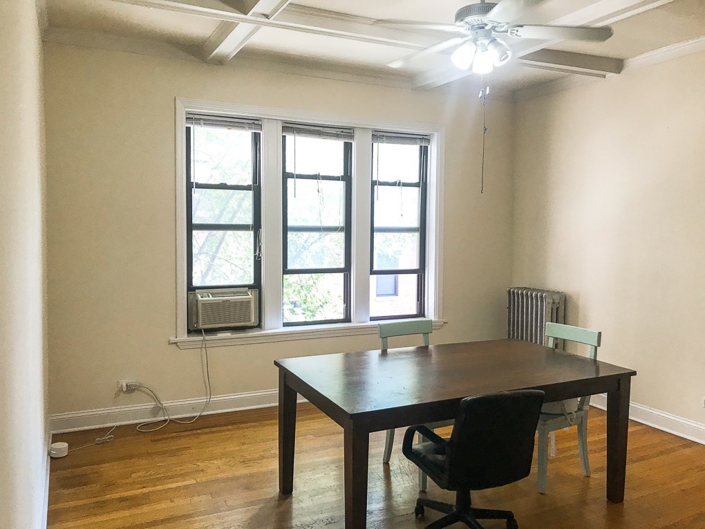 A room with a table and chairs and a window with an air conditioner.