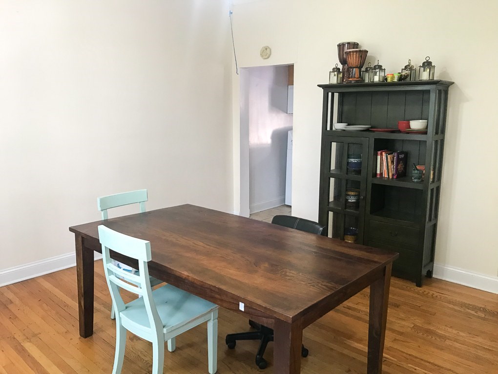 A wooden table with a blue chair in front of a black bookshelf.