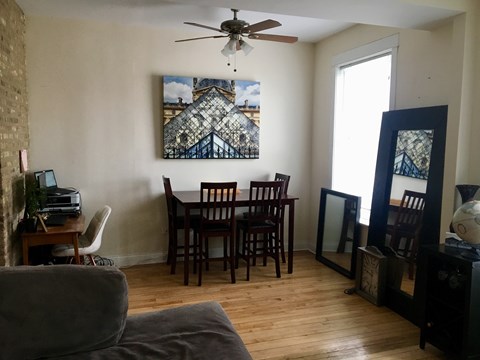 A room with a ceiling fan, a dining table with chairs, and a painting on the wall.