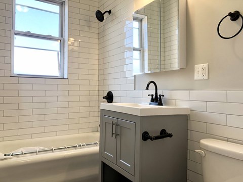 A bathroom with a white tub, sink, and grey cabinet.
