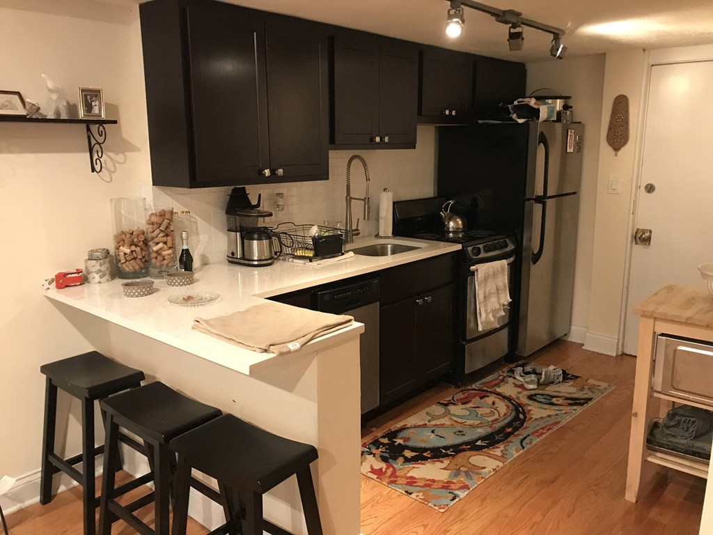 a small kitchen with black cabinets and a counter with three stools