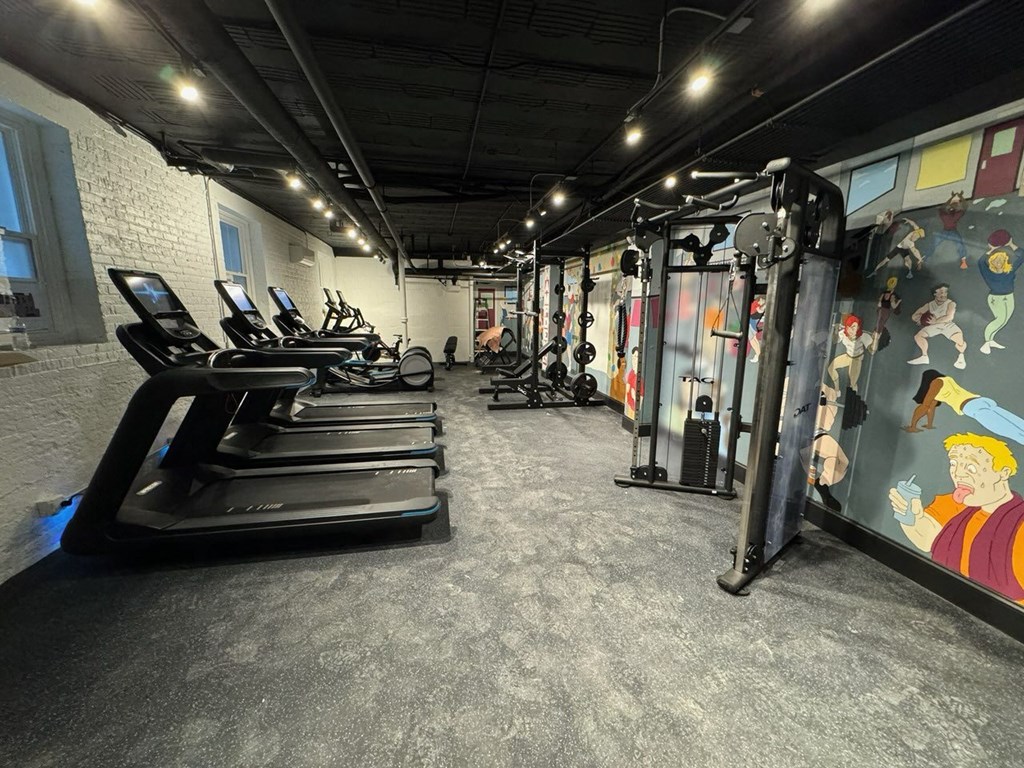 a gym with cardio equipment and a wall mural of the beatles on the wall