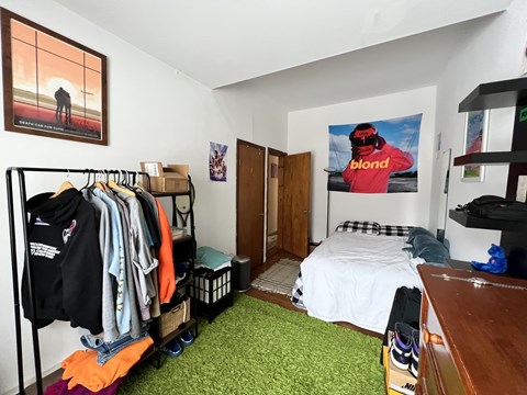 A room with a bed, a clothing rack, and a poster on the wall.