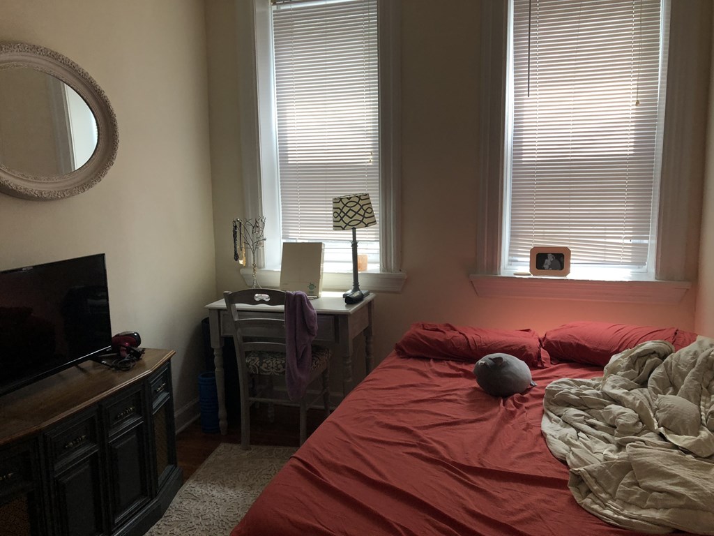 A bedroom with a red bedspread and a grey blanket.