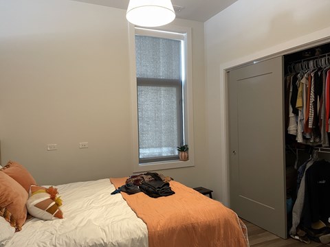 A bedroom with a bed, a window with a curtain, and a wardrobe with clothes.