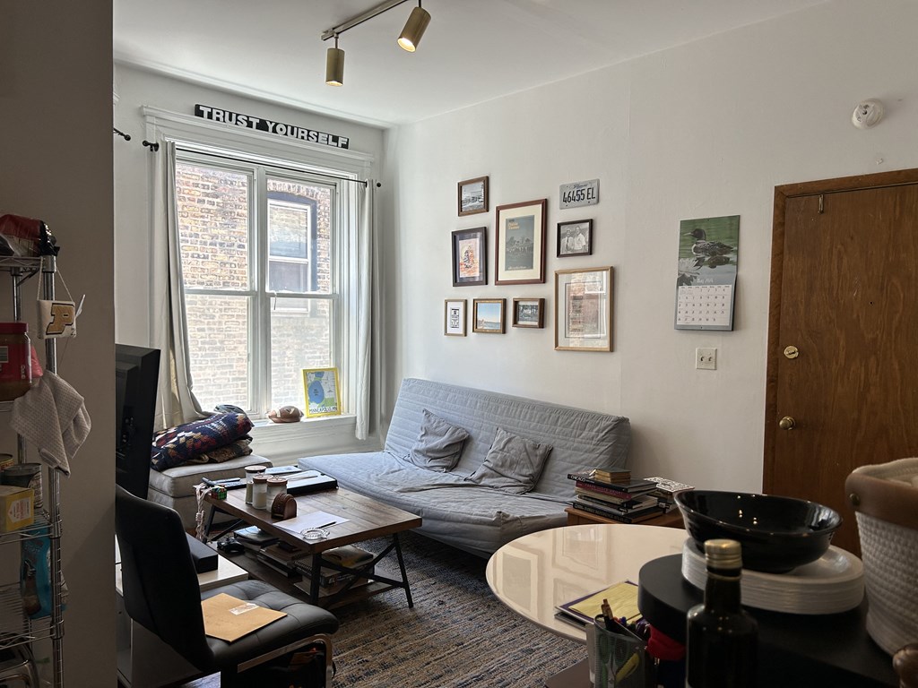 A living room with a grey couch, a coffee table, and a window with a view of a brick building outside.