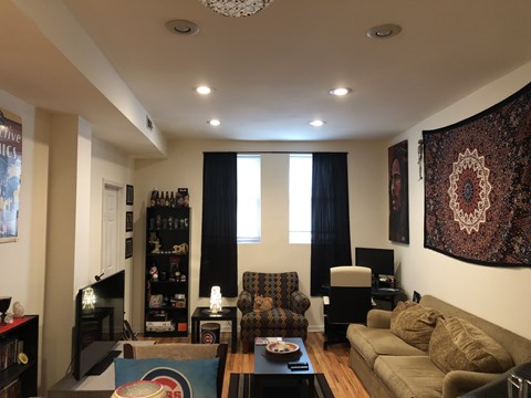 A living room with a brown couch, a coffee table, and a large tapestry on the wall.