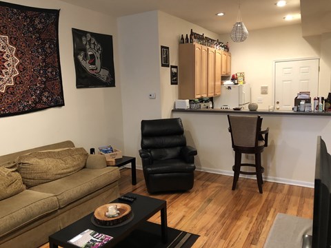 A living room with a brown couch, a black chair, and a coffee table with a bowl of food on it.