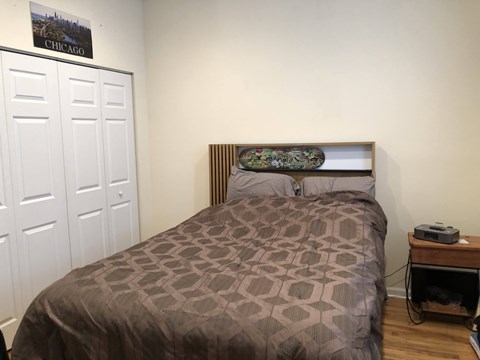 A bed with a brown patterned comforter sits in a room with a white door and a poster on the wall.