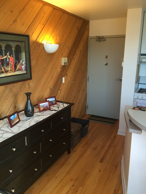 A room with a wooden ceiling and a black dresser with a vase on top.