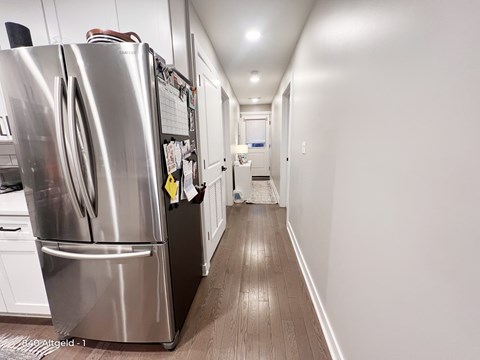 A stainless steel refrigerator is in a narrow hallway.