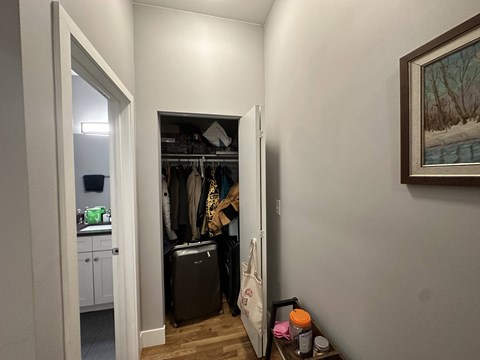A room with a doorway leading to a closet with clothes hanging and a suitcase on the floor.