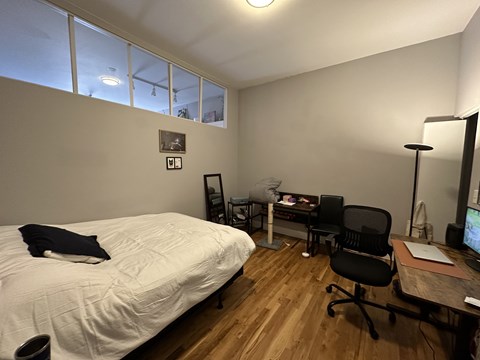 A bedroom with a bed, desk, chair, and a window.