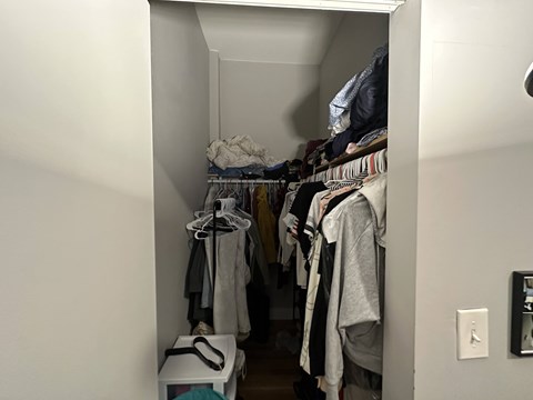 A small closet with clothes hanging on hangers.