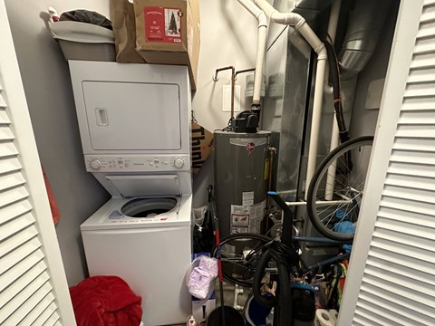 A white dryer and washer are in a small, cluttered laundry room.