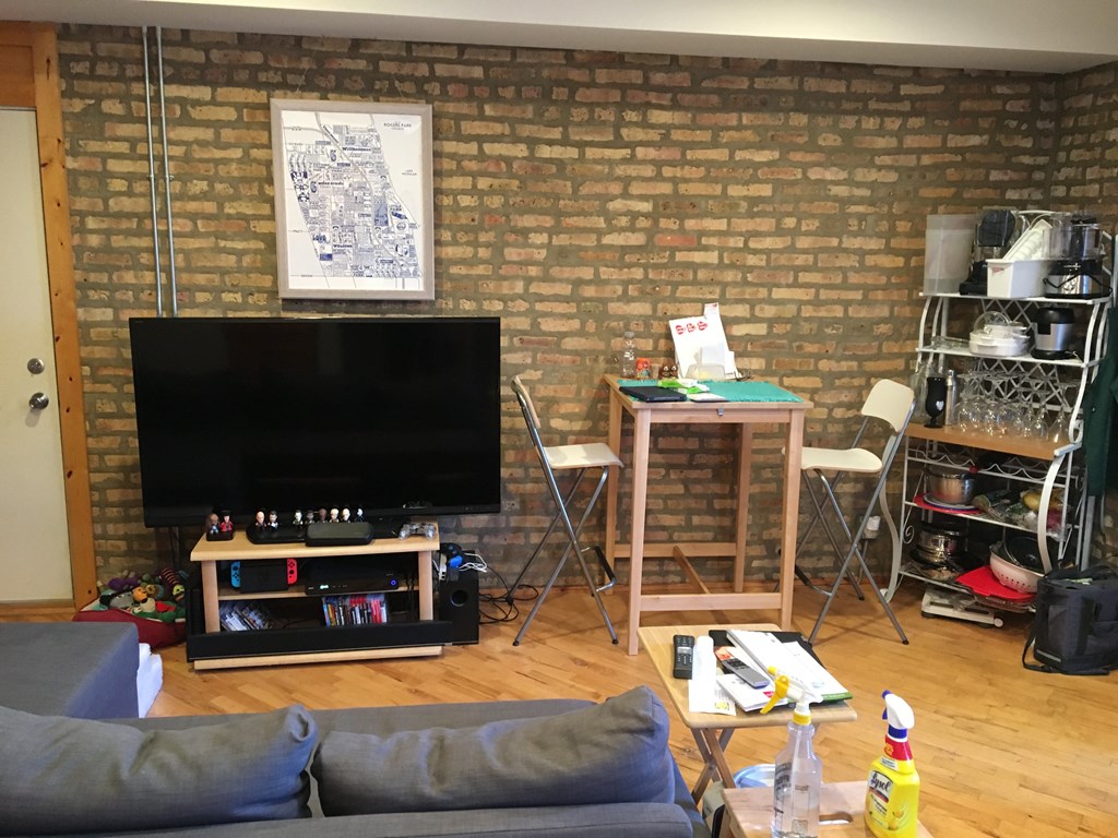 A living room with a grey couch, a black television, and a brick wall.