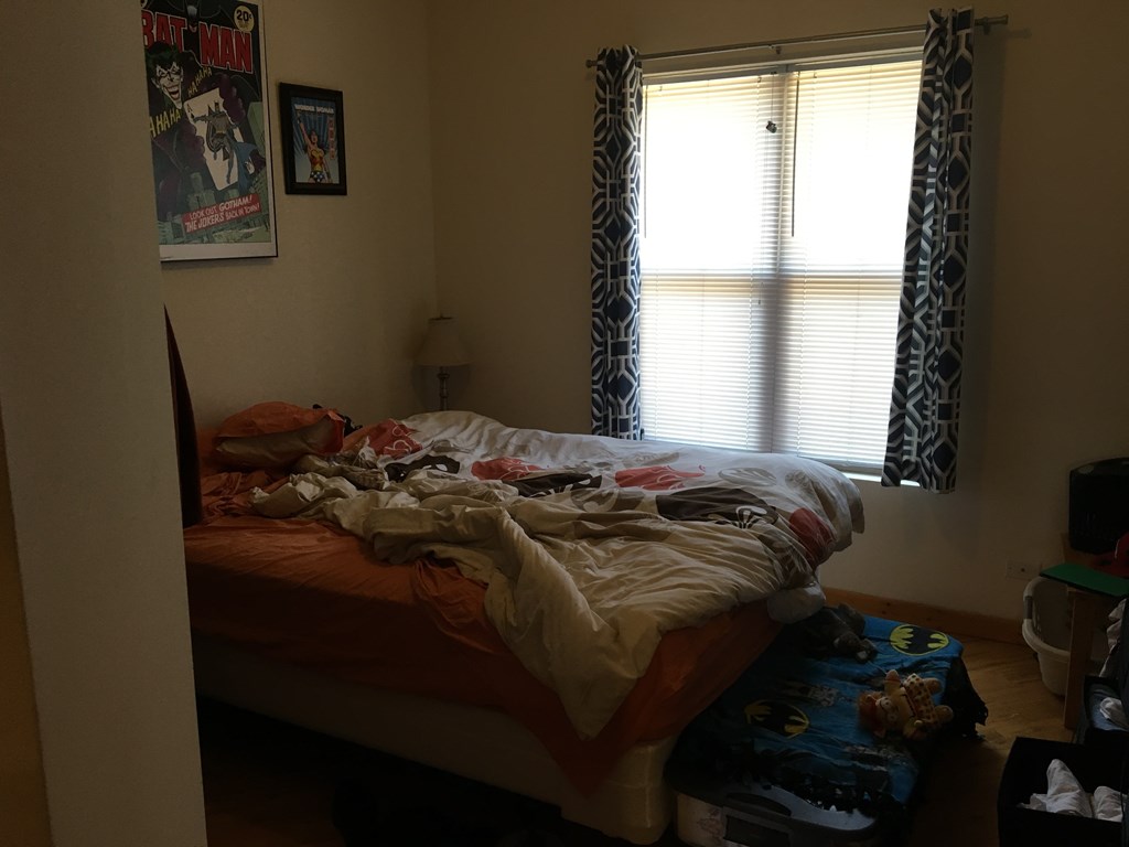 A messy bedroom with a bed in the center and a poster on the wall.