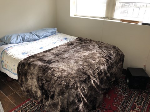 A bed with a blue pillow and a black box on the floor.
