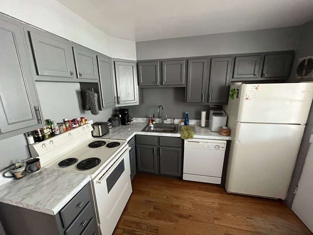 A kitchen with white appliances and wooden floors.