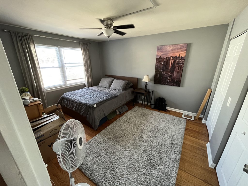 A bedroom with a bed, a fan, and a painting on the wall.