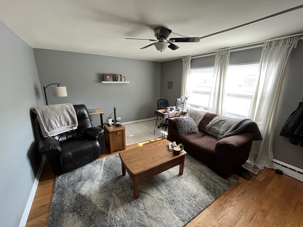 A living room with a black leather chair, a brown couch, a wooden coffee table, and a ceiling fan.