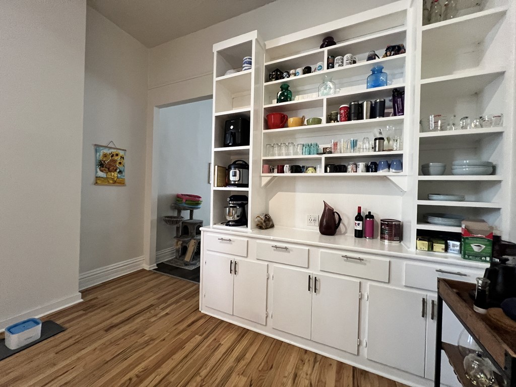 a kitchen with white cabinets and shelves and a wood floor