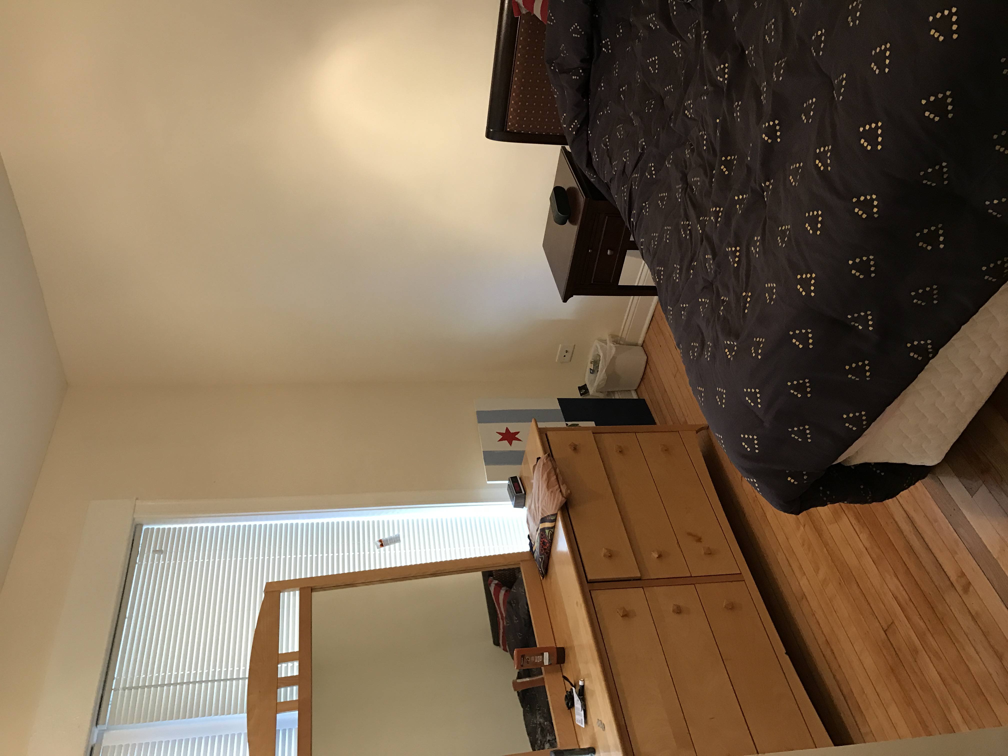 A bedroom with a bed, wooden cabinet, and a window with blinds.