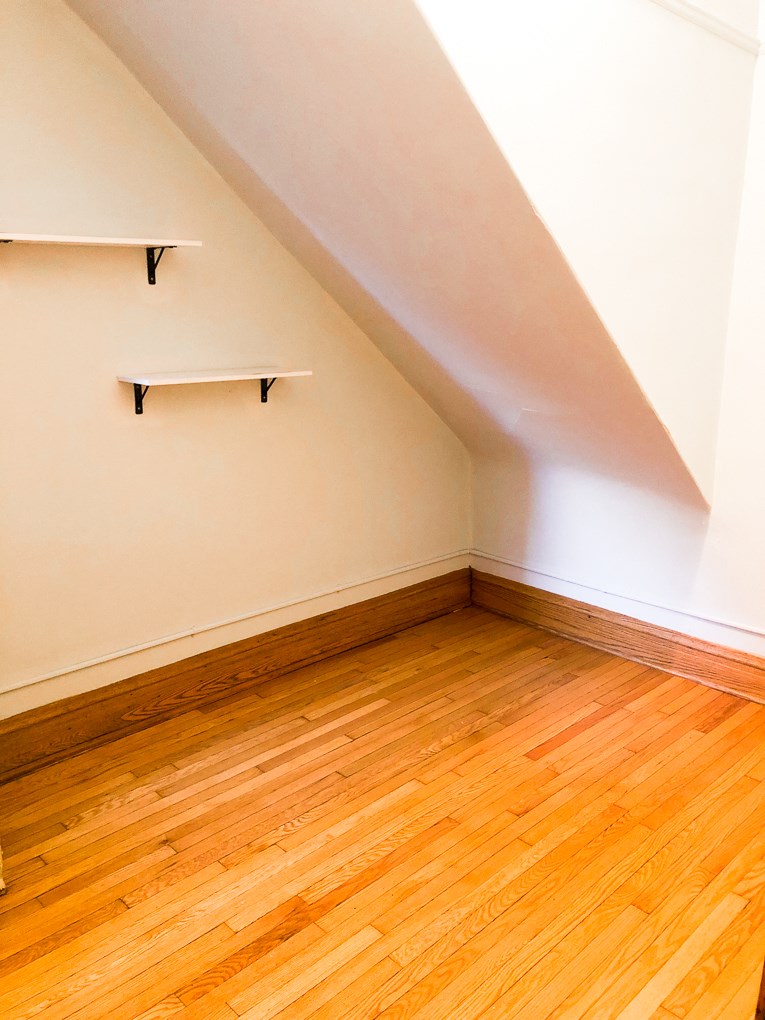 an empty room with wooden floors and a shelf on the wall