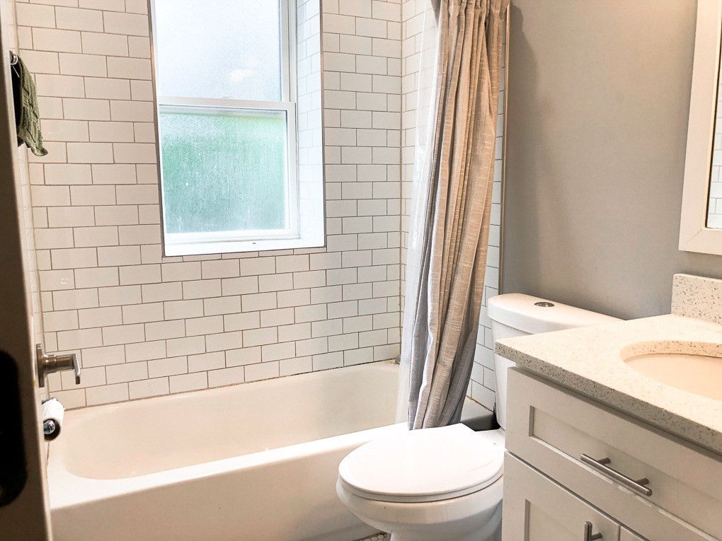 A white toilet sits next to a bathtub in a bathroom with a window.