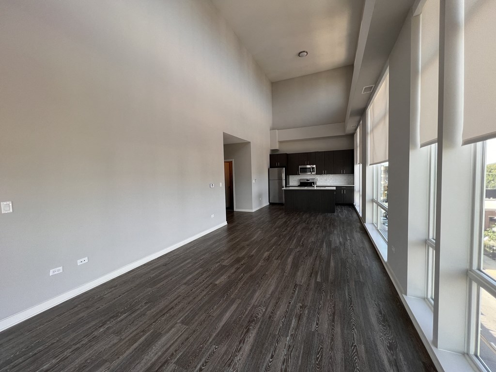 an empty living room with a large window and a kitchen
