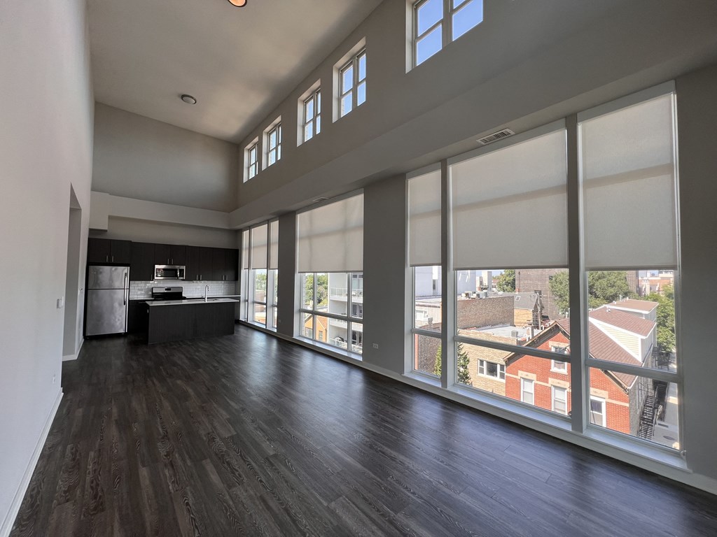 an empty living room with large windows and a kitchen