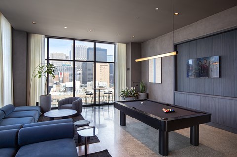A pool table is in the middle of a room with a couch and a plant.