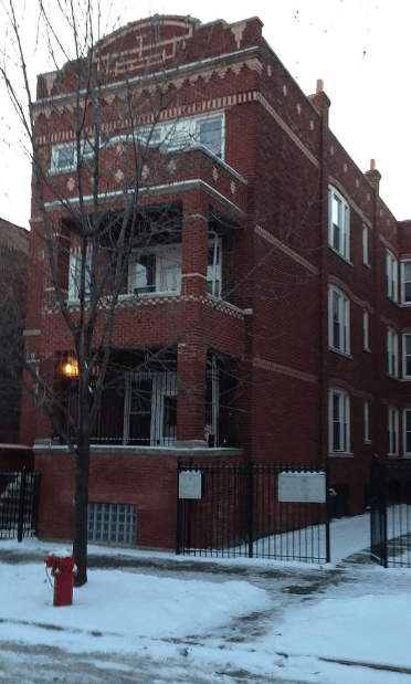 A red brick building with a black fence and a red fire hydrant in front of it.
