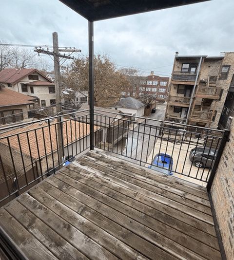 A balcony with a wooden floor and metal railing overlooks a residential area.