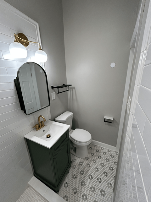 A bathroom with a toilet, sink, mirror and light fixture.