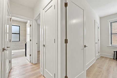 A hallway with white doors and a window with blinds.
