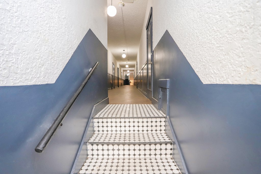 a long hallway with stairs and blue and white tiles and a metal railing