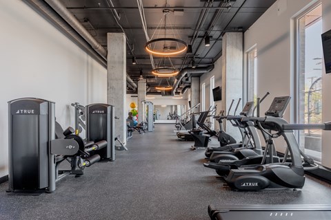 A gym with a row of treadmilers and elliptical machines.