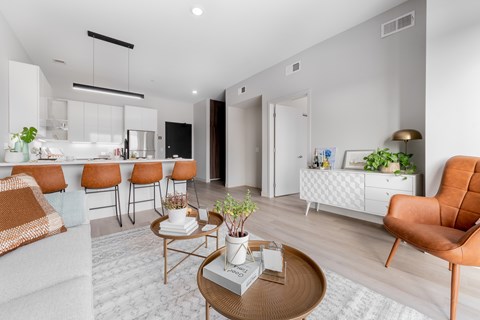 A modern living room with a white kitchen in the background.