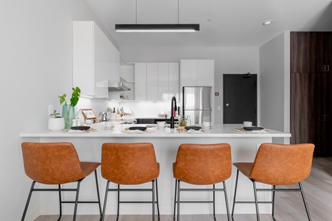 A modern kitchen with white cabinets and a long island with four chairs.