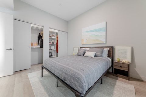 A bedroom with a bed, nightstand, and a painting on the wall.