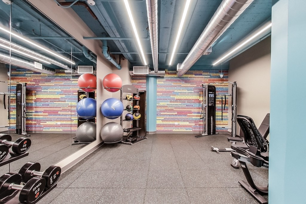 a workout room with weights and balls and a wall of colorful tiles