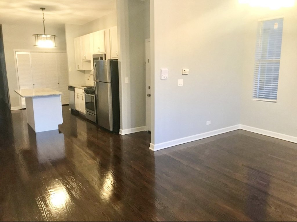 an empty living room with wood floors and a kitchen