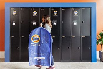 a woman walks past a row of gray lockers with a blue bag in front of her