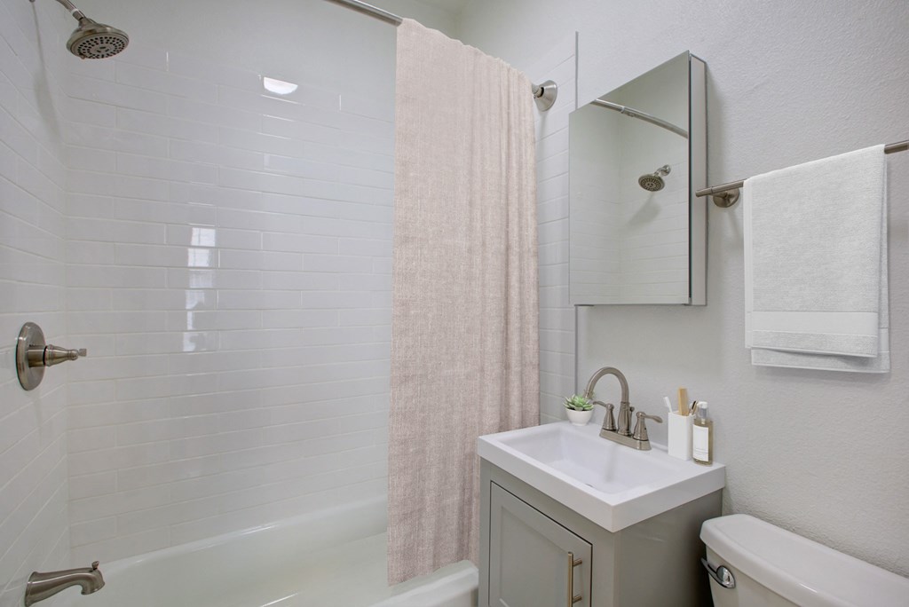 a bathroom with a white sink and tub and a white toilet with a pink shower curtain